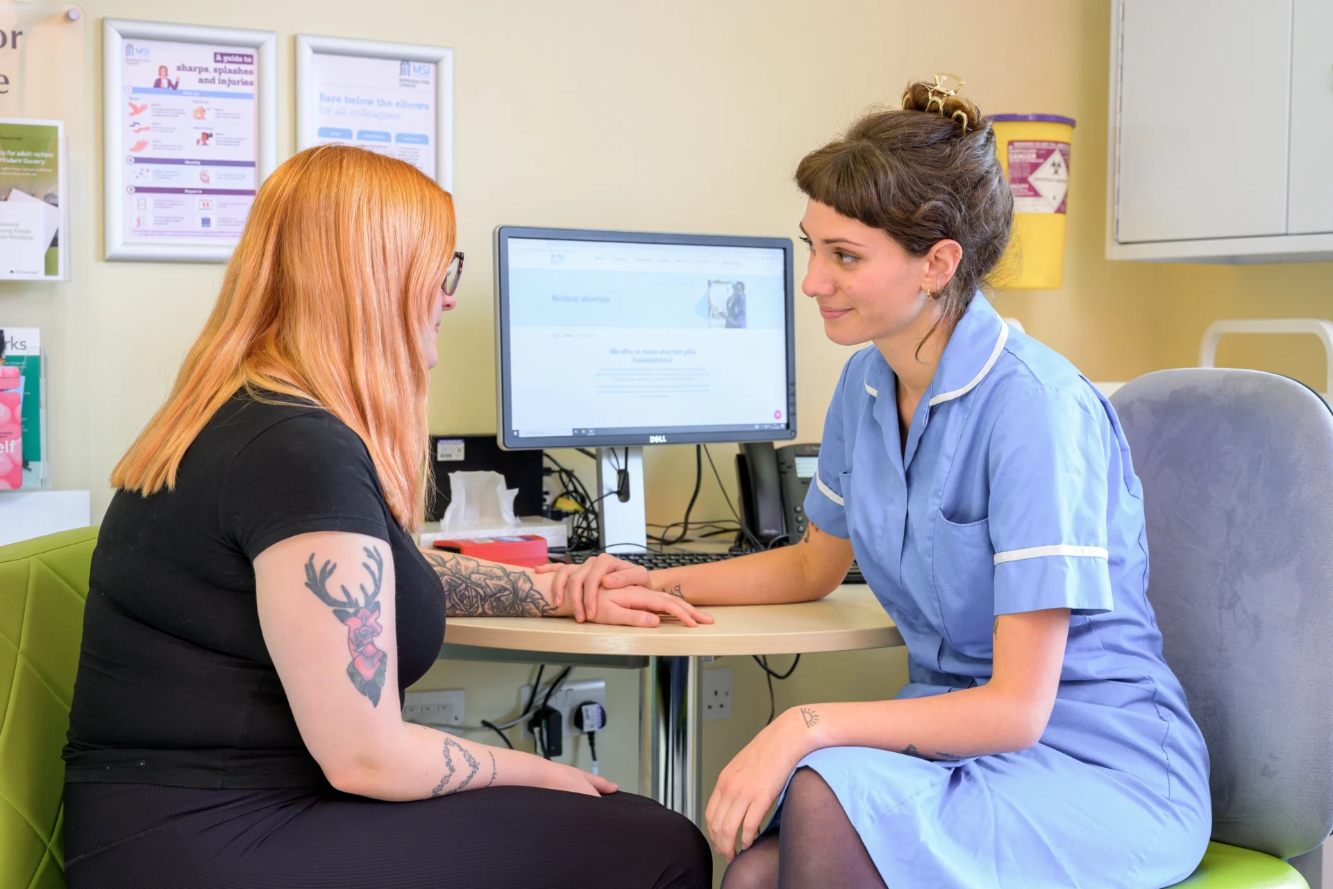 An MSI nurse holding a client's hand whilst they are sat at a table in a consultation room.